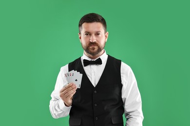 Professional croupier with playing cards on green background