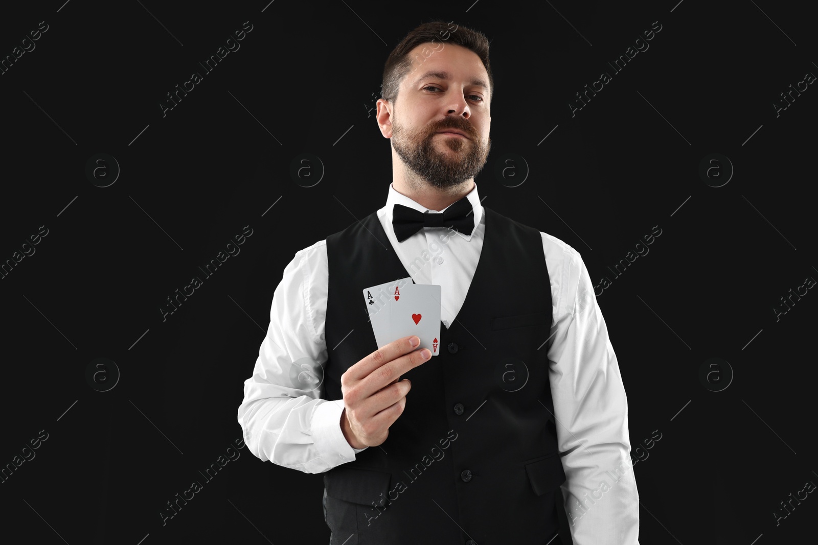 Photo of Professional croupier with playing cards on black background