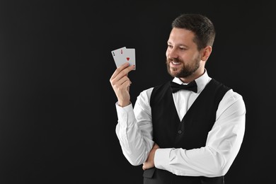 Photo of Professional croupier with playing cards on black background, space for text