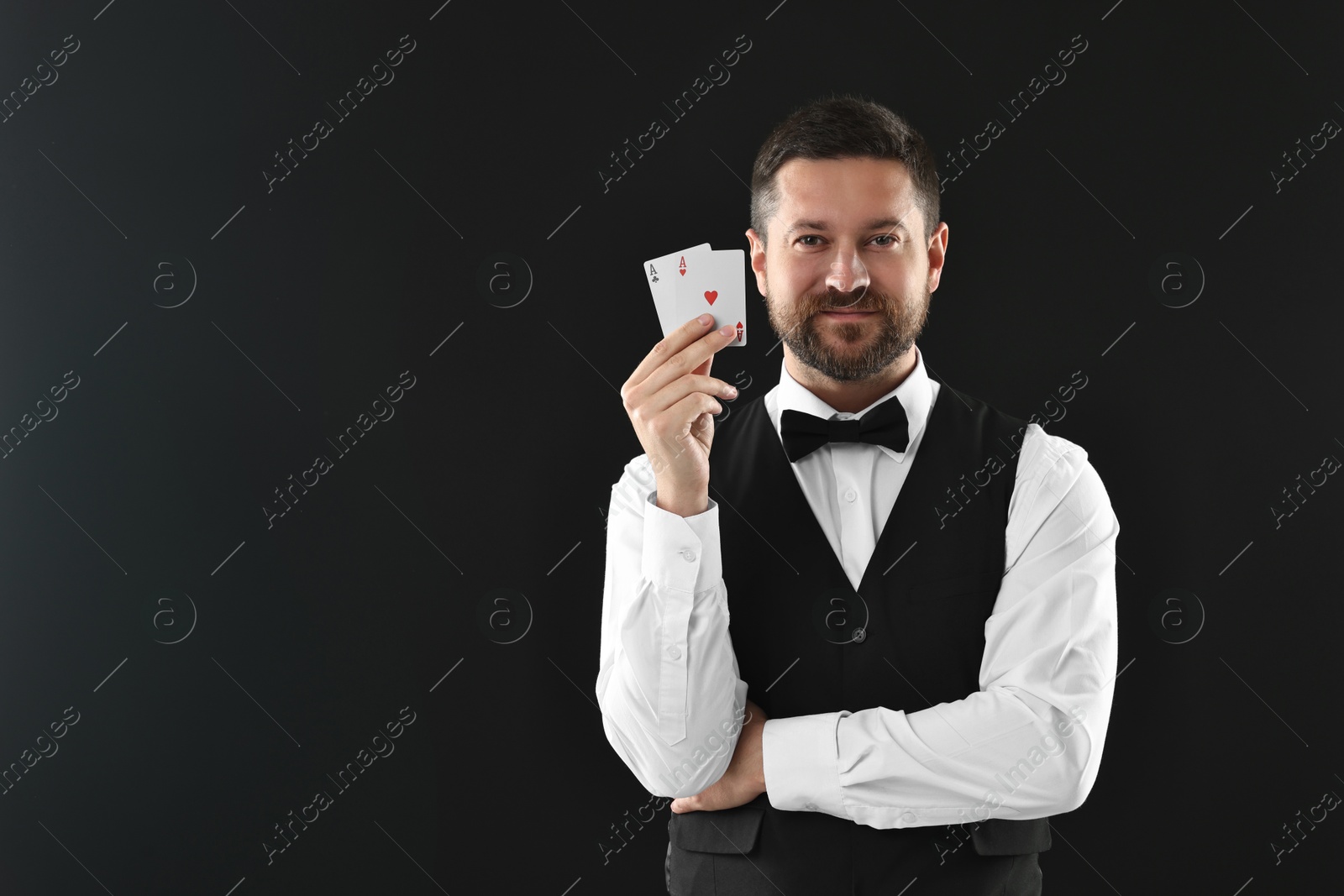 Photo of Professional croupier with playing cards on black background, space for text