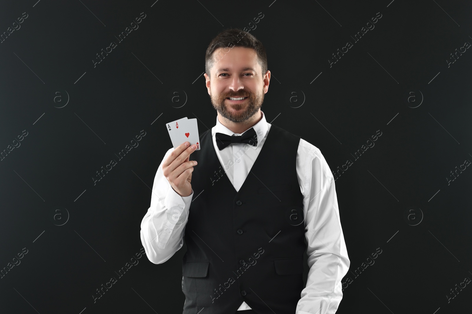 Photo of Professional croupier with playing cards on black background