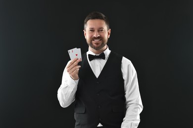 Professional croupier with playing cards on black background