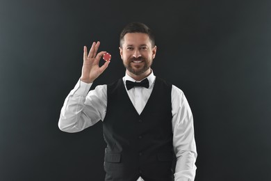 Croupier with casino chip on black background