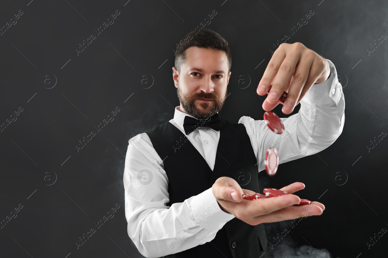 Photo of Croupier holding casino chips on black background with smoke