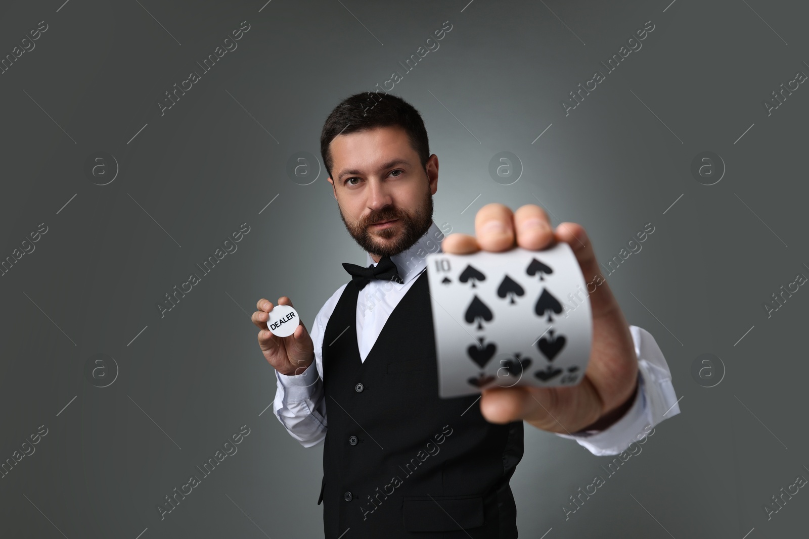 Photo of Croupier holding card and dealer button on grey background