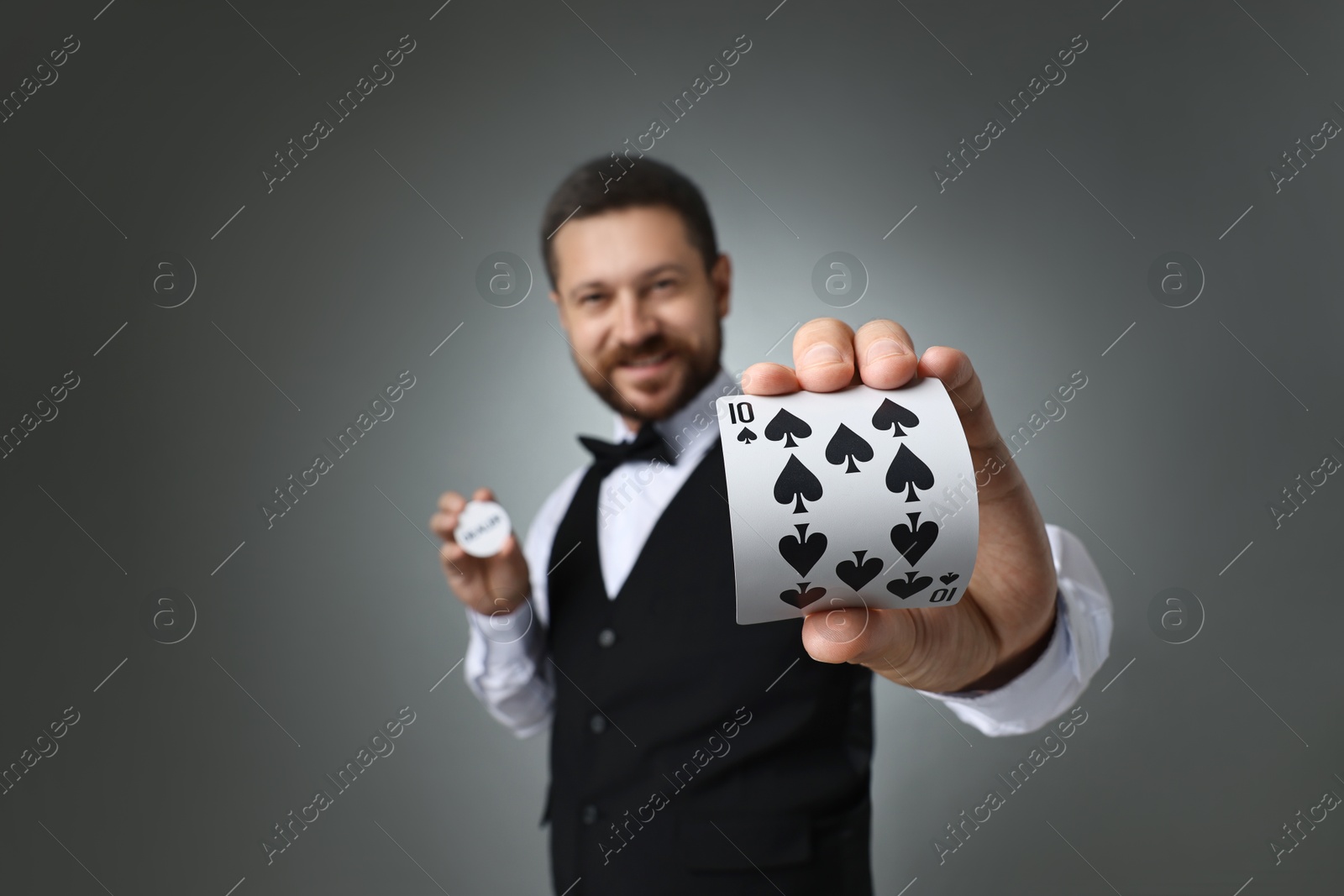 Photo of Croupier holding card and dealer button on grey background, selective focus