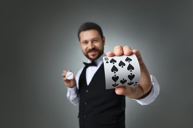 Croupier holding card and dealer button on grey background, selective focus