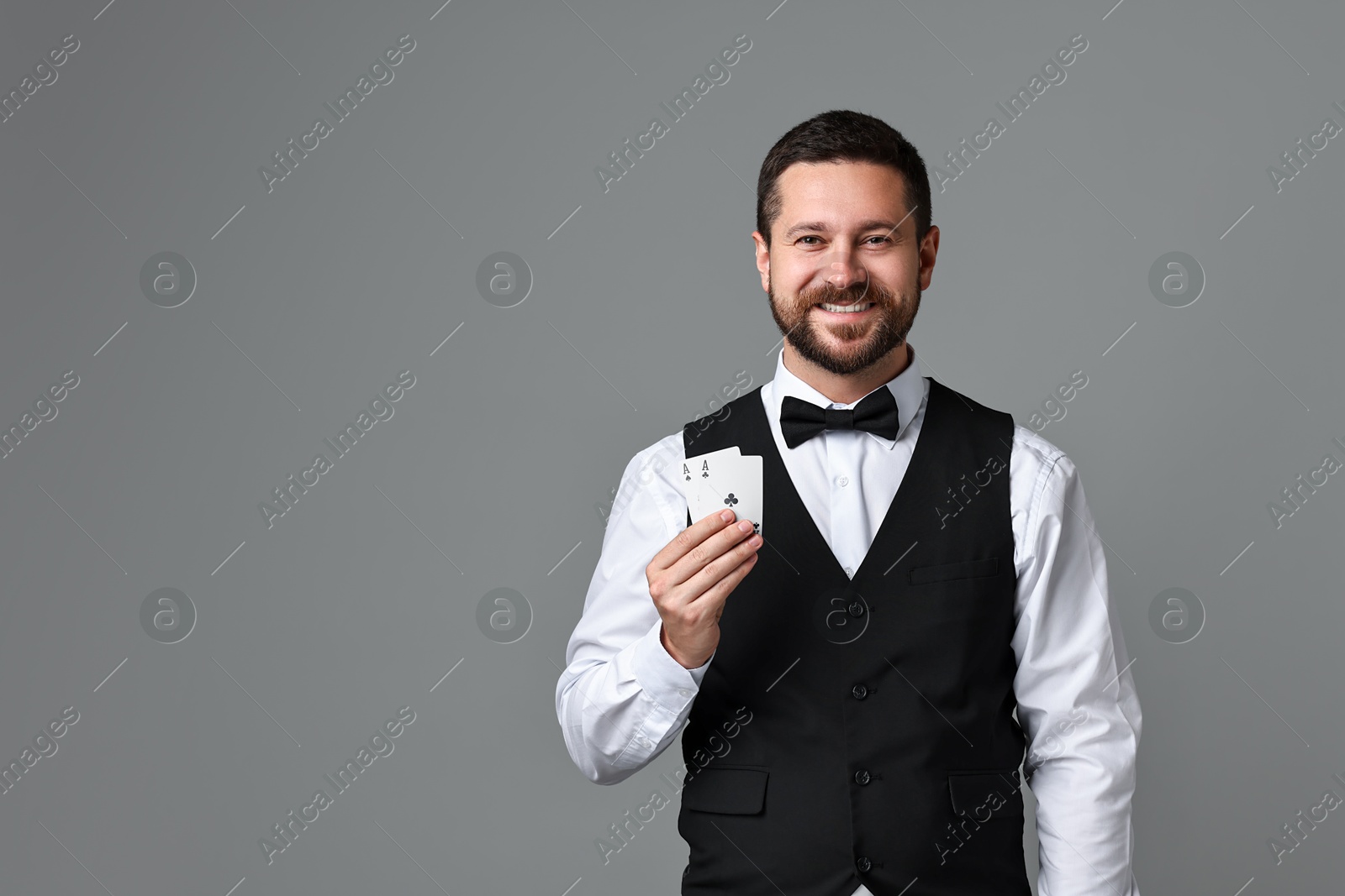 Photo of Professional croupier with playing cards on grey background, space for text