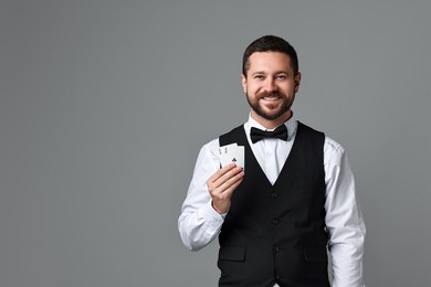 Professional croupier with playing cards on grey background, space for text