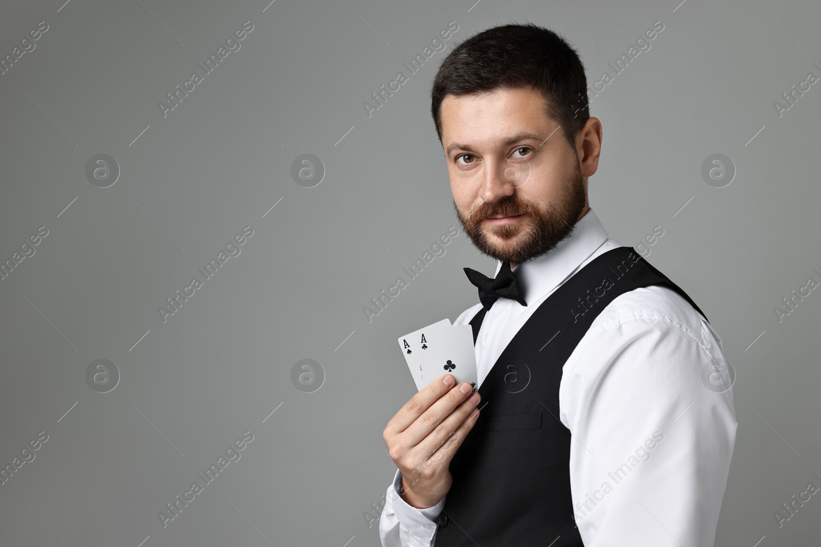 Photo of Professional croupier with playing cards on grey background, space for text