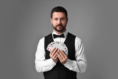 Professional croupier with playing cards on grey background