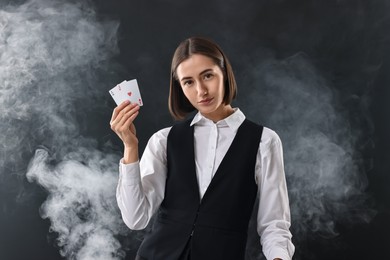 Croupier holding playing cards on black background with smoke