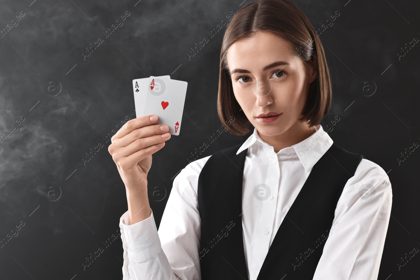 Photo of Croupier holding playing cards on black background with smoke