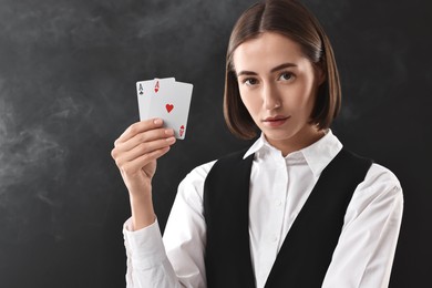 Croupier holding playing cards on black background with smoke