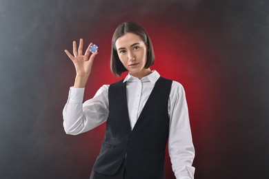 Photo of Croupier holding casino chip on dark red background with smoke