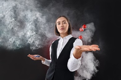 Croupier holding casino chips and dice on dark red background with smoke