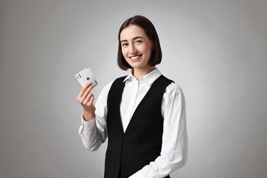 Professional croupier with playing cards on grey background