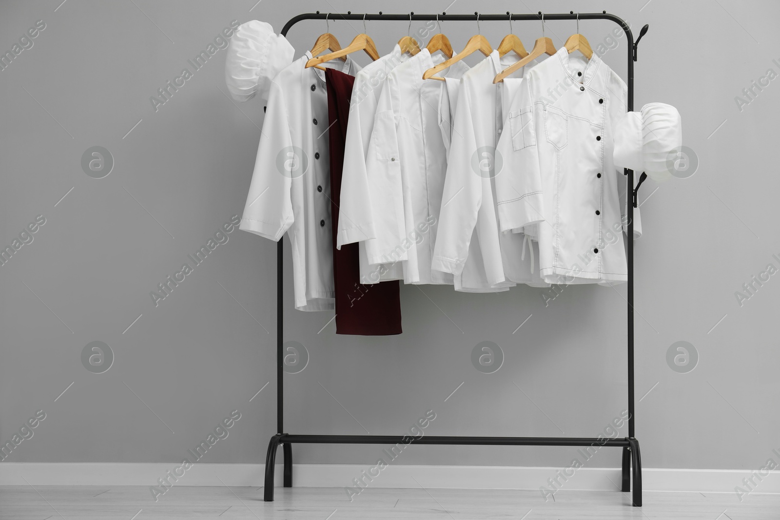 Photo of Chefs' uniforms on clothing rack near grey wall indoors. Space for text