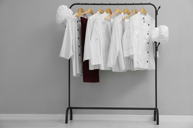 Photo of Chefs' uniforms on clothing rack near grey wall indoors. Space for text