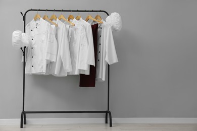 Photo of Chefs' uniforms on clothing rack near grey wall indoors. Space for text