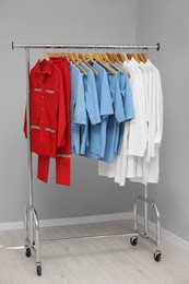 Different medical workers' uniforms on clothing rack near grey wall indoors