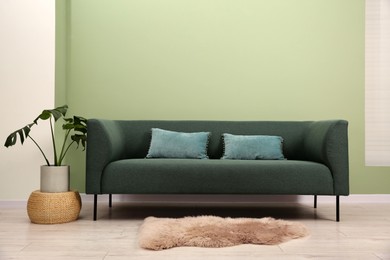 Stylish sofa with pillows, houseplant and lamp near green wall indoors