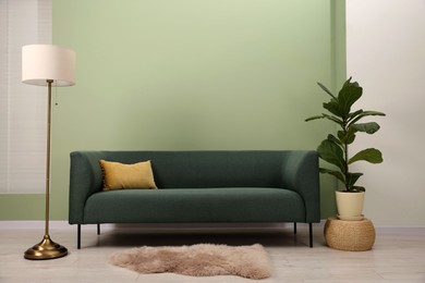 Stylish sofa with pillow, houseplant and lamp near green wall indoors