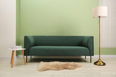 Photo of Stylish sofa, side table and lamp near green wall indoors