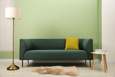 Photo of Stylish sofa with pillow, side table and lamp near green wall indoors