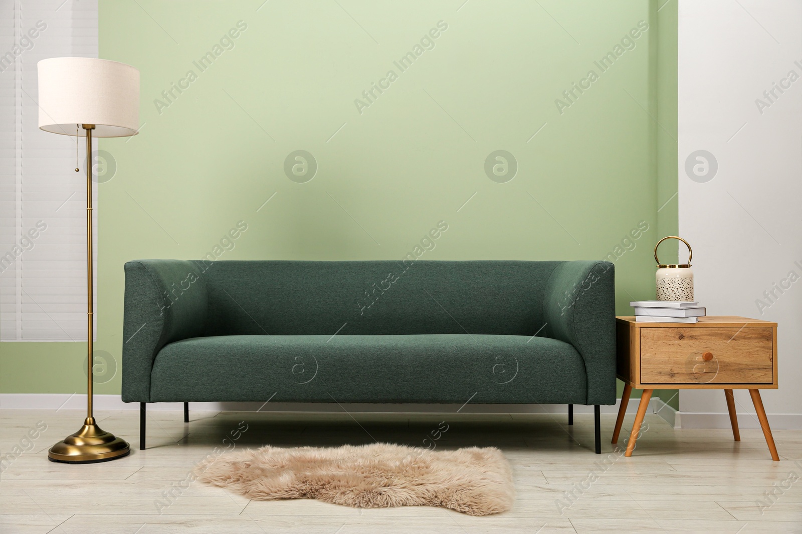 Photo of Stylish sofa, side table and lamp near green wall indoors