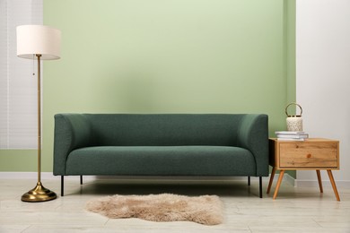 Photo of Stylish sofa, side table and lamp near green wall indoors