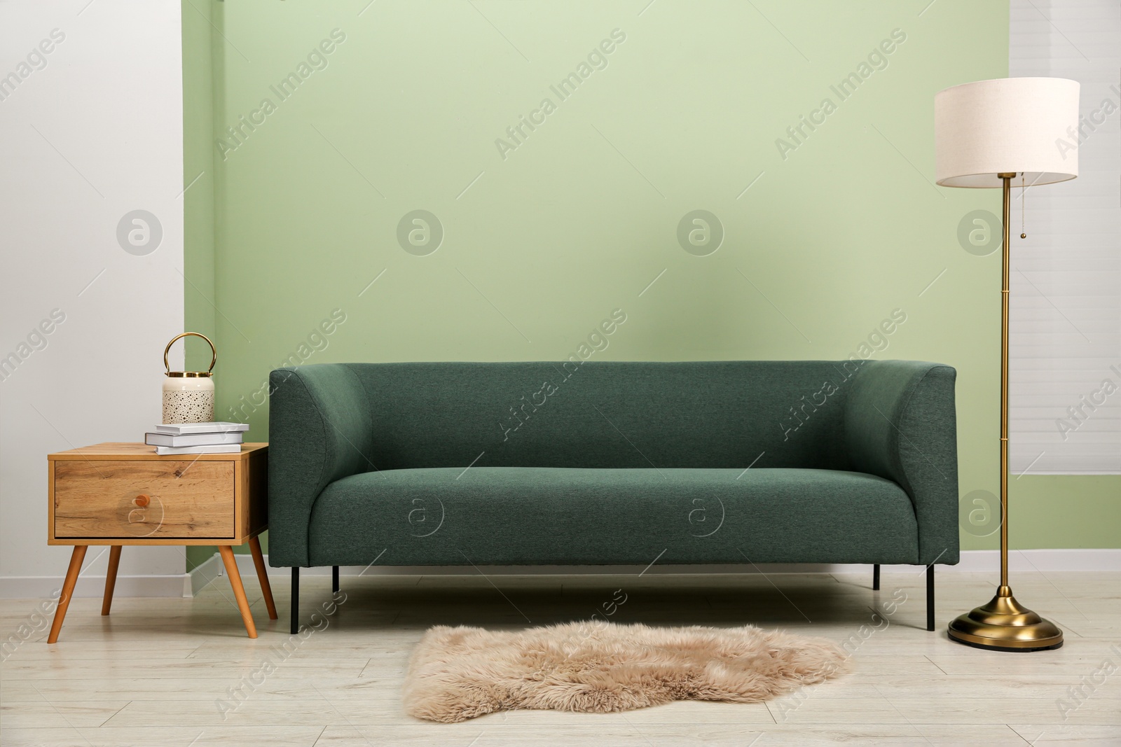 Photo of Stylish sofa, side table and lamp near green wall indoors