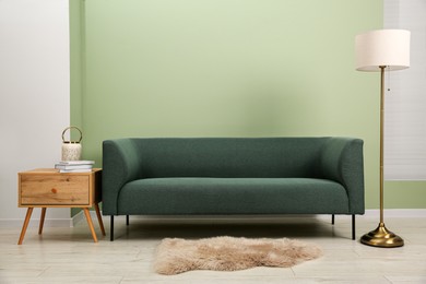 Stylish sofa, side table and lamp near green wall indoors