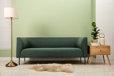 Stylish sofa, houseplant, side table and lamp near green wall indoors