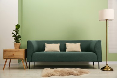 Stylish sofa, houseplant, side table and lamp near green wall indoors