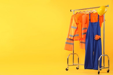 Photo of Workers' uniforms on clothing rack against yellow background. Space for text