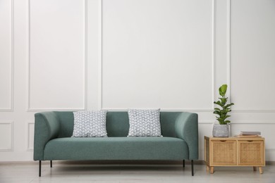 Stylish sofa with cushions, plant and books on side table near white wall