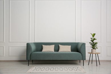 Photo of Stylish sofa, pillows and side table with houseplant near white wall indoors