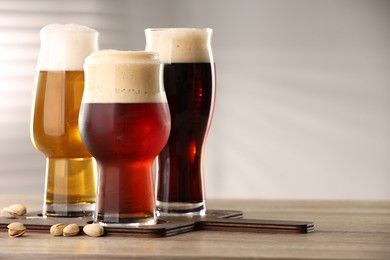 Photo of Glasses with different types of beer and pistachio nuts on wooden table indoors, space for text