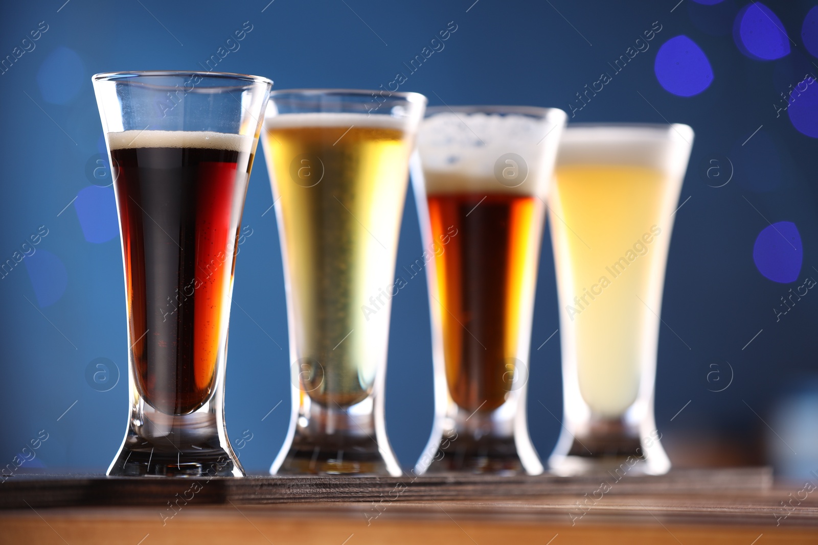 Photo of Glasses with different types of beer on wooden table against blue background, closeup