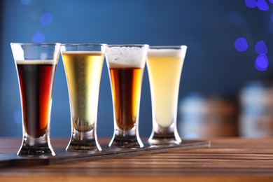 Photo of Glasses with different types of beer on wooden table against blue background, closeup