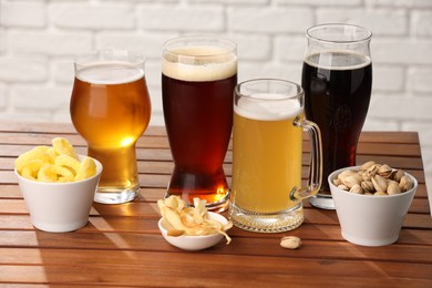 Photo of Glasses with different types of beer and snacks on wooden table against white brick wall