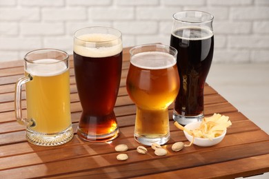 Photo of Glasses with different types of beer and snacks on wooden table against white brick wall