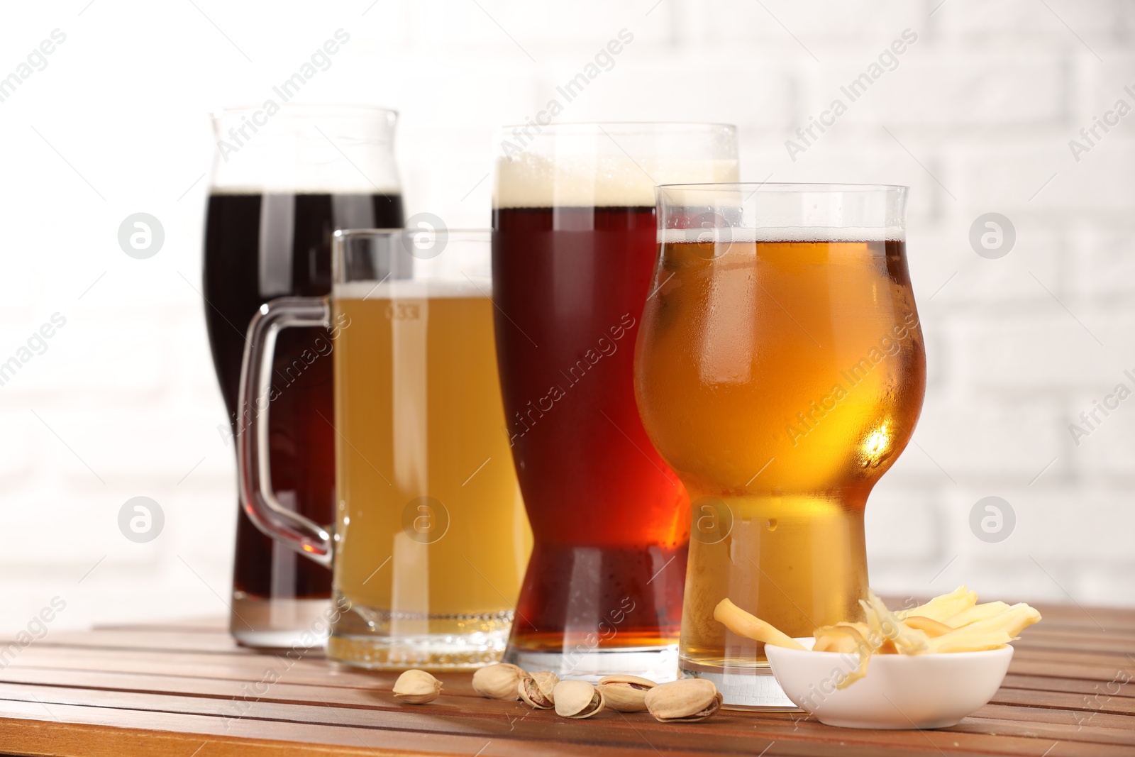 Photo of Glasses with different types of beer and snacks on wooden table against white wall, closeup