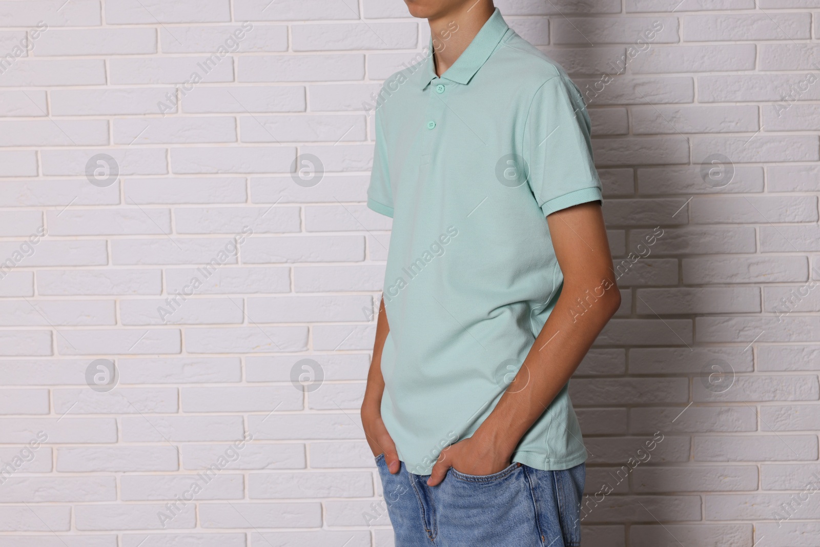 Photo of Teenage boy wearing light green t-shirt near white brick wall, closeup. Space for text