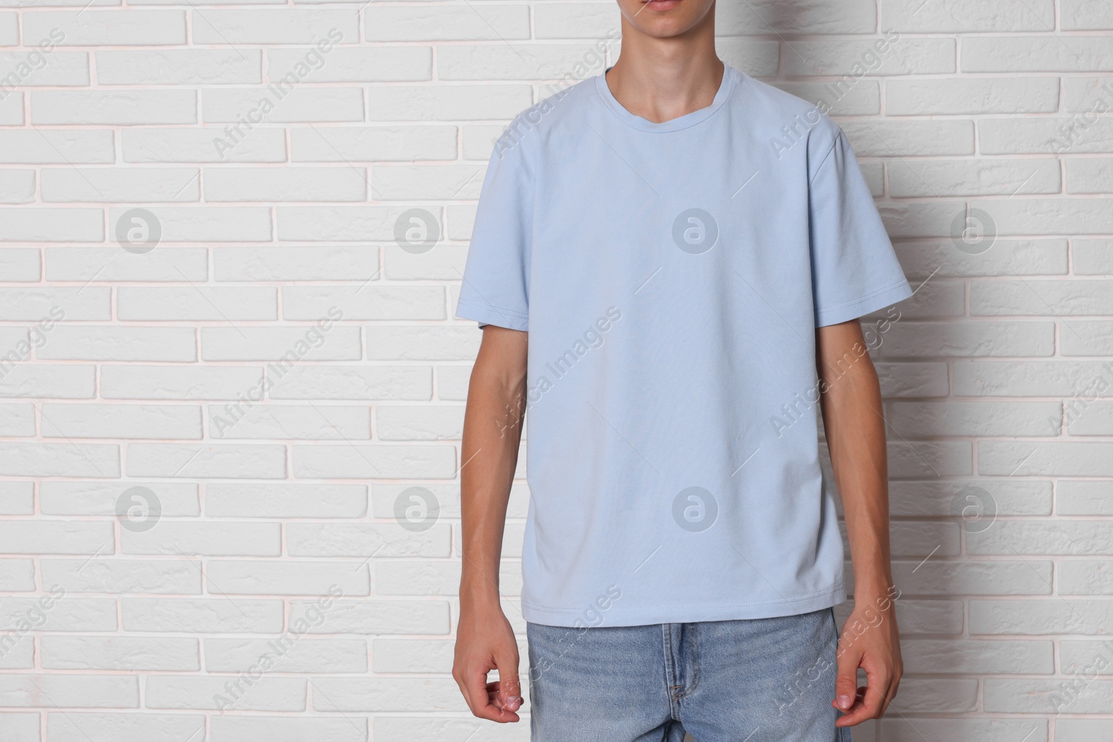 Photo of Teenage boy wearing light blue t-shirt near white brick wall, closeup. Space for text