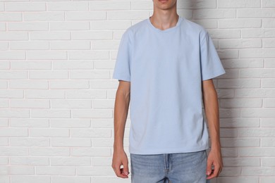 Photo of Teenage boy wearing light blue t-shirt near white brick wall, closeup. Space for text