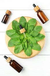 Photo of Tinctures in bottles, pipette and mint on white wooden table, top view