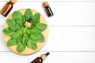 Photo of Tinctures in bottles, pipette and mint on white wooden table, top view. Space for text