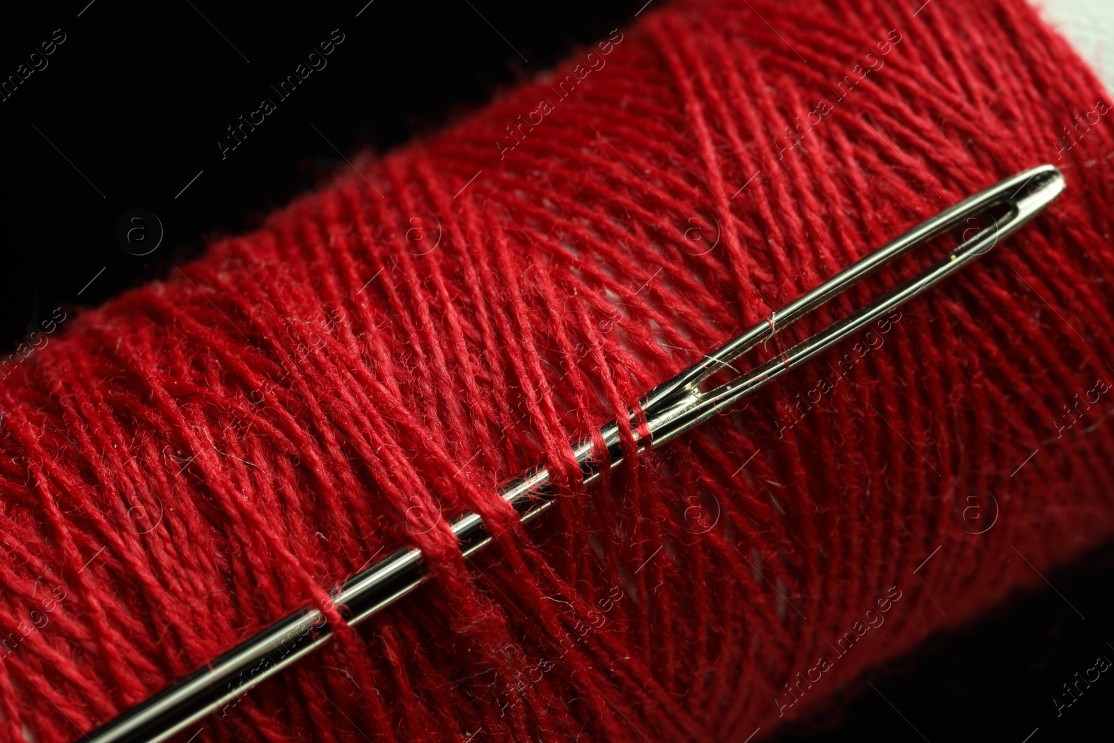 Photo of Spool of red sewing thread with needle on black background, closeup